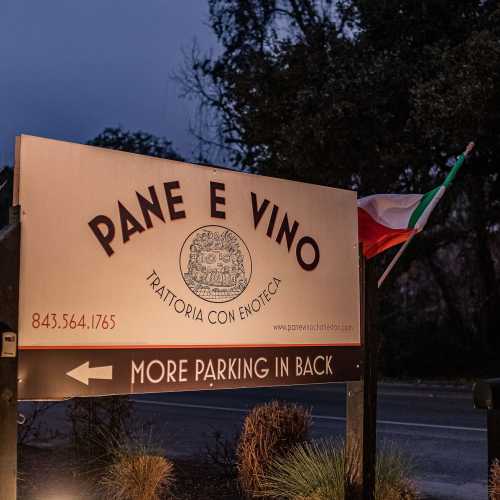 Sign for Pane e Vino restaurant with Italian flag, indicating more parking in back. Evening setting.