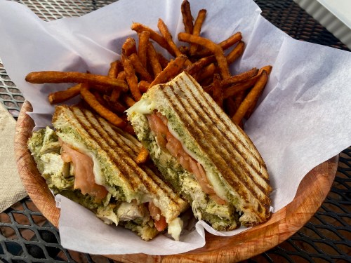 A grilled sandwich with tomato and pesto, served with a side of crispy sweet potato fries in a basket.