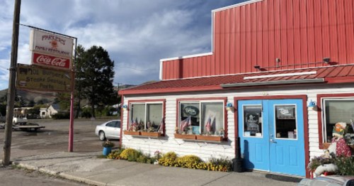 A quaint restaurant with a red roof and blue door, featuring flower boxes and a vintage Coca-Cola sign outside.