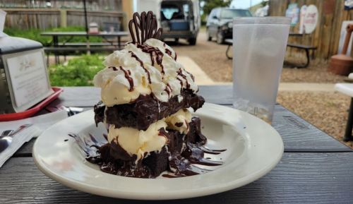 A towering dessert of chocolate cake layered with ice cream, drizzled with chocolate sauce and topped with a chocolate garnish.