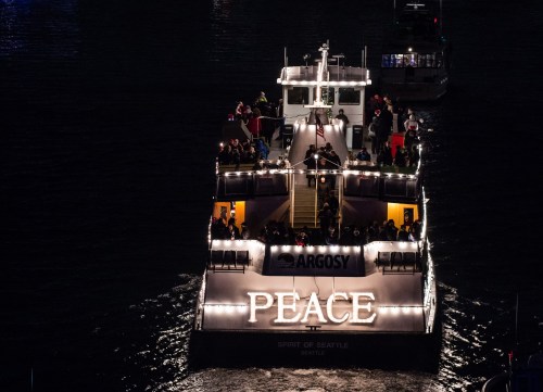 A boat named "Peace" illuminated at night, with passengers enjoying the view on a calm waterway.