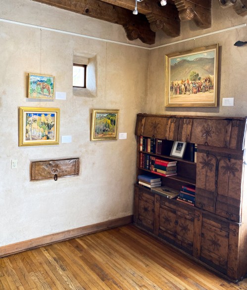 A cozy corner of a room featuring framed paintings on the wall and a wooden bookshelf filled with books.