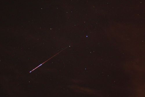 A bright meteor streaks across a dark night sky filled with stars.