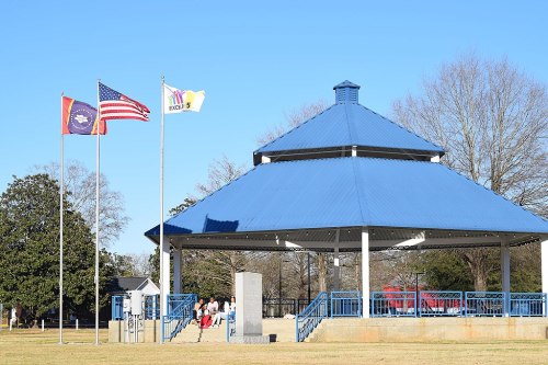 A blue gazebo in a park with flags, including the U.S. flag, against a clear blue sky.