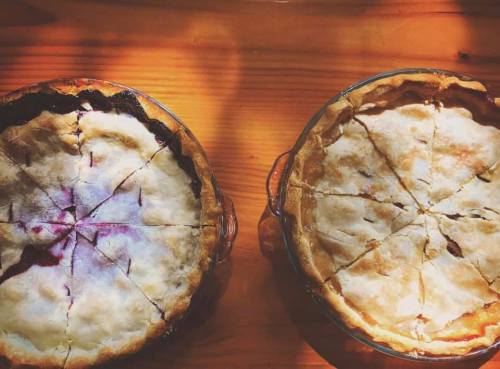 Two freshly baked pies on a wooden table, one with a dark berry filling and the other with a light fruit filling.