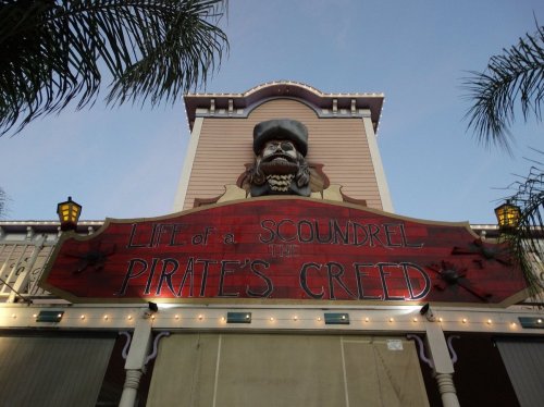 Sign for "Life of a Scoundrel: The Pirate's Creed" featuring a pirate figure, set against a blue sky.