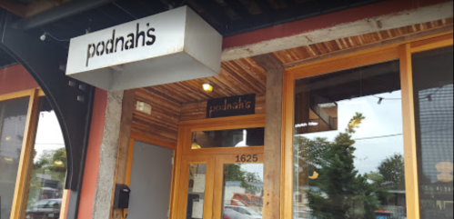 Exterior of Podnah's restaurant, featuring a wooden door and sign, with a modern design and urban surroundings.