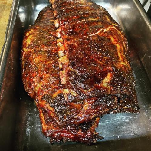 A large, perfectly cooked rack of ribs with a smoky, caramelized glaze, resting in a metal tray.