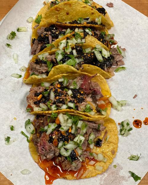 A close-up of five tacos filled with meat, topped with onions, cilantro, and sauce, served on parchment paper.