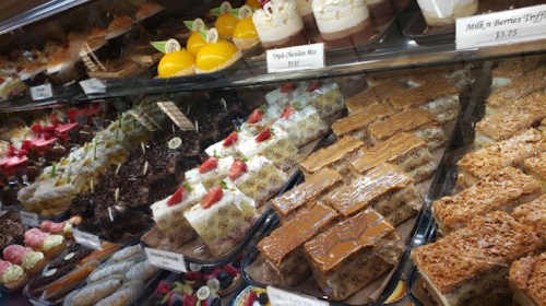 A display case filled with various colorful desserts, including cakes, pastries, and layered treats.