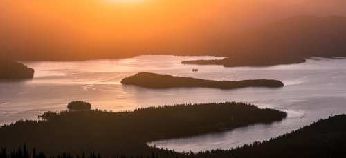 A serene landscape at sunset, featuring islands and calm waters reflecting warm orange hues.