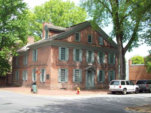 Historic brick building with green shutters, surrounded by trees, located at a street corner.