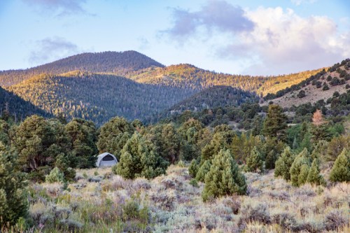A serene landscape featuring mountains, trees, and a tent nestled in a grassy area under a colorful sky.