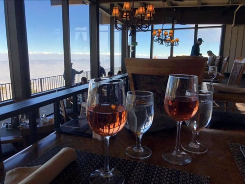 A table set with glasses of rosé and water, overlooking a scenic mountain view through large windows.