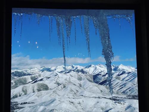 Icicles hang from a window, framing a snowy mountain landscape under a clear blue sky.