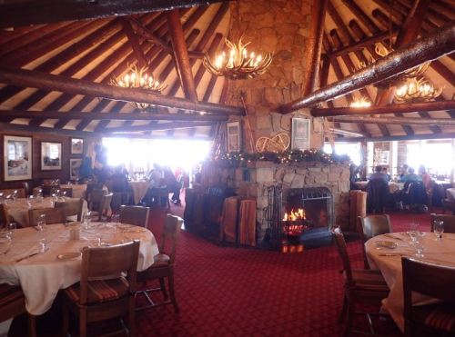 Cozy restaurant interior with a stone fireplace, wooden beams, and tables set for dining, creating a warm atmosphere.