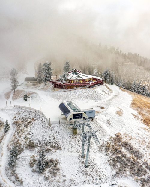 A snowy mountain landscape featuring a ski lodge and a chairlift surrounded by fog and pine trees.