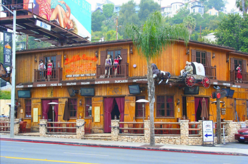 A rustic wooden building with balconies, featuring a horse-drawn carriage and outdoor seating, surrounded by greenery.