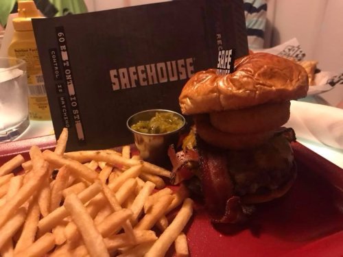 A gourmet burger with bacon and cheese, topped with onion rings, served with fries and a side of pickles.