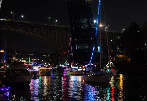 Colorful boats decorated with lights on a river at night, with a bridge partially raised in the background.