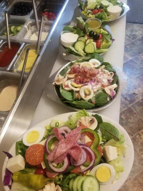 A variety of colorful salads with greens, vegetables, cheese, and dressings arranged on a counter.