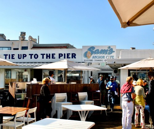 Outdoor dining area at Sam's Anchor Cafe, with people enjoying the atmosphere and umbrellas providing shade.
