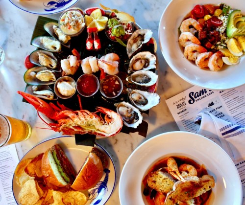 A seafood feast featuring oysters, shrimp, lobster, and a variety of dishes, with drinks and menus on a table.