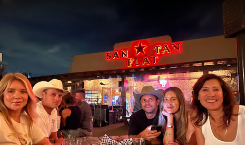 A group of five friends poses for a photo outside San Tan Flat restaurant at night, with a vibrant sign in the background.