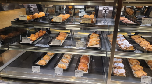 A display case filled with various baked goods, including pastries and pies, labeled with names and prices.