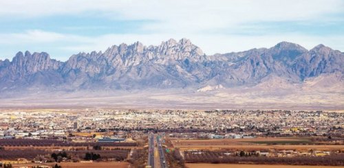 A panoramic view of a city with mountains in the background and a road leading into the distance.