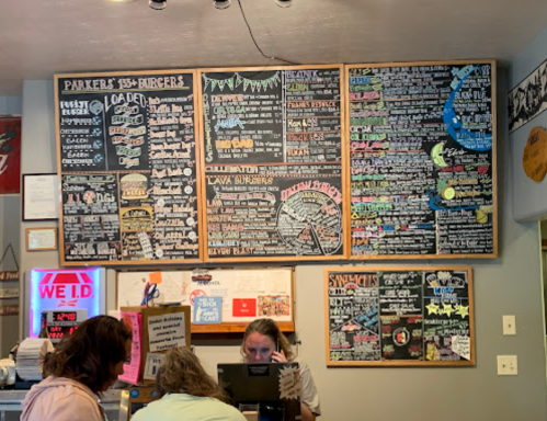 A menu board with various burger options and specials, displayed in a casual dining setting. Two customers are seated.