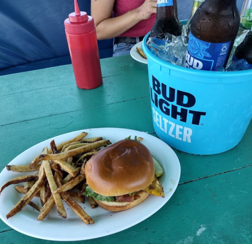 A plate with a burger and fries next to a bucket of Bud Light Seltzer bottles on a green table.