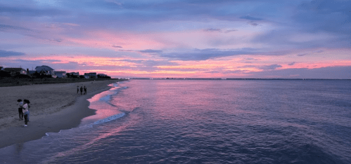 A serene beach at sunset, with soft waves lapping the shore and people walking along the water's edge.
