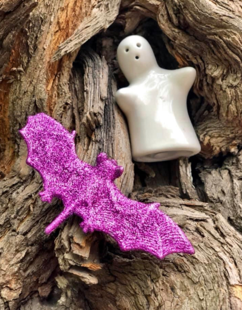 A shiny purple bat and a small white ghost figure resting on textured tree bark.