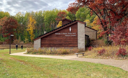 A wooden visitor center surrounded by colorful autumn trees and a walking path in William O'Brien State Park.