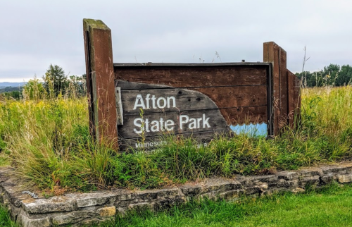 Sign for Afton State Park, surrounded by tall grass and trees, with a cloudy sky in the background.