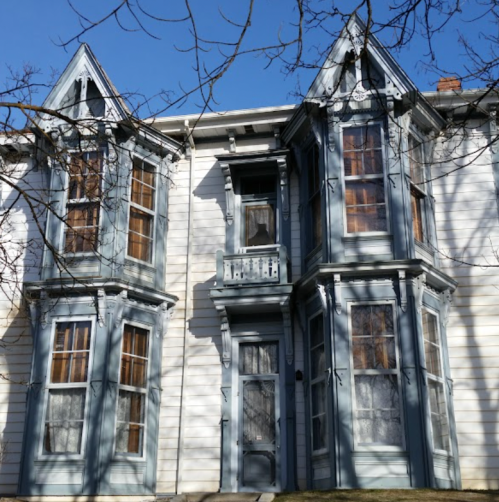 Victorian-style house with blue trim, featuring bay windows and intricate architectural details against a clear blue sky.