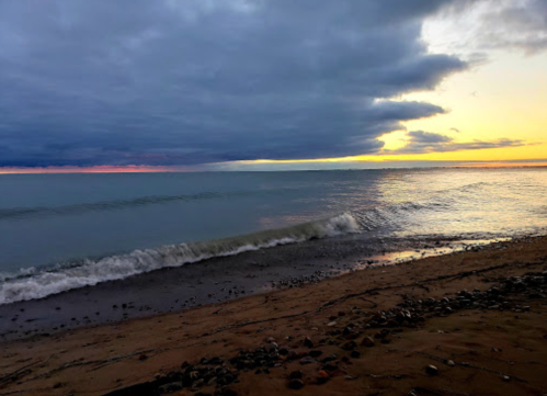 A serene beach scene at sunset, with gentle waves lapping at the shore under a cloudy sky.