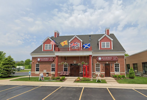 A brick restaurant with flags, featuring a red phone booth and a welcoming entrance, set against a cloudy sky.