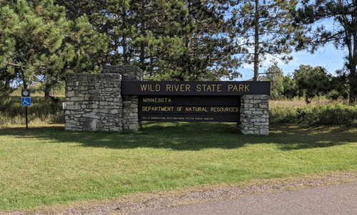 Sign for Wild River State Park in Minnesota, featuring stone pillars and surrounded by trees and grass.