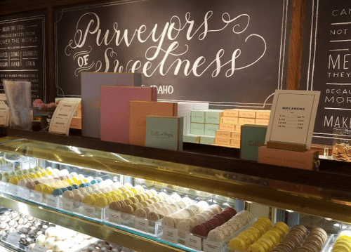 A display of colorful macarons and sweet treats in a shop, with a decorative sign reading "Purveyors of Sweetness."