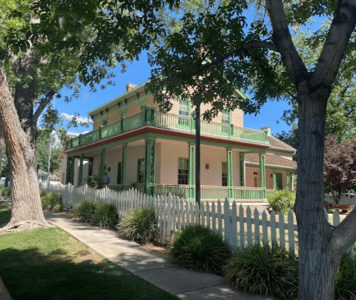 A two-story house with green trim and a white picket fence, surrounded by trees and a well-maintained lawn.