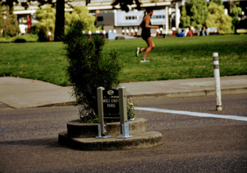 Sign for Mill End Park in a green area, with a person jogging in the background.