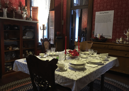 A vintage dining room set with a table laid for a meal, featuring elegant dishware and decorative candles.