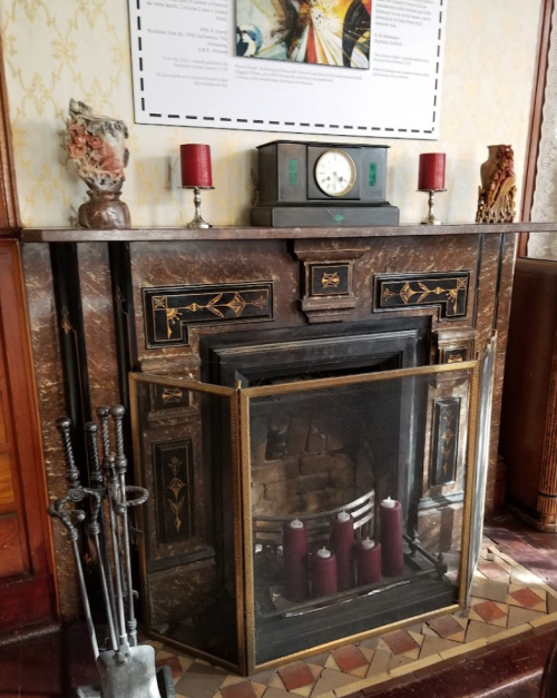 A decorative fireplace with a clock, candles, and ornate details, set against a patterned wall.