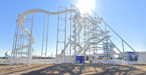 A large, white water slide structure with multiple twisting slides under a clear blue sky.
