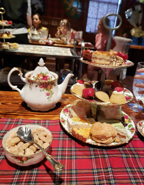 A beautifully arranged afternoon tea set with a teapot, tiered desserts, and a bowl of sugar on a tartan tablecloth.