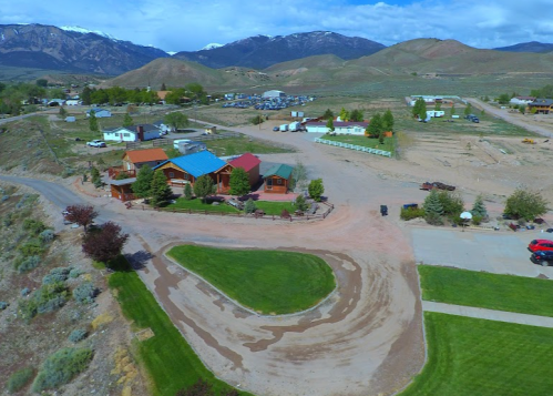 Aerial view of a rural area with houses, a winding road, and mountains in the background under a blue sky.