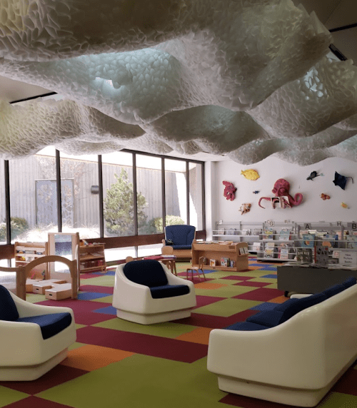 A colorful children's library with cloud-like decor, seating areas, and bookshelves filled with books.