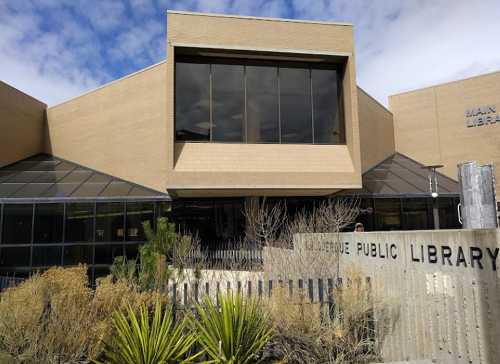 Exterior of a modern public library building with large windows and desert landscaping.